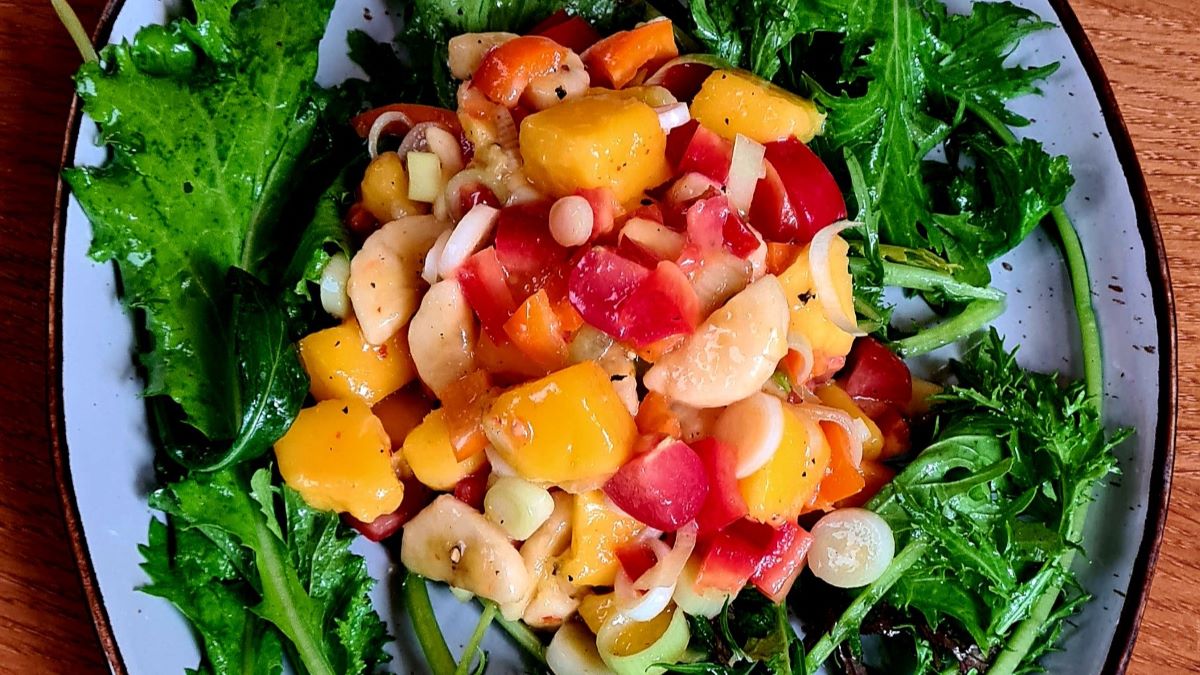 Tropischer Salat, der die Sonne aufgehen lässt: Auf Salatblättern liegen die bunten Zutaten.