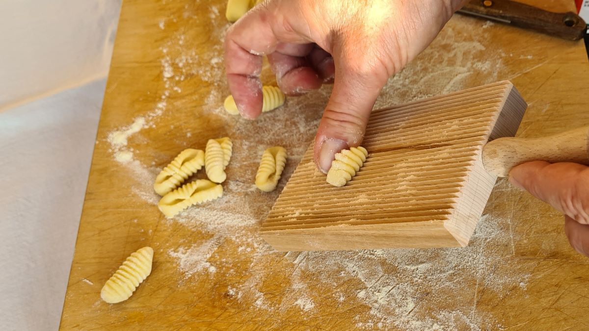 Cavatelli formen: Das Bild zeigt eine Riga-Gnocchi (ein Gnocchi-Brett mit Rillen), über das Teigstücke gerollt werden, um Cavatelli zu erzeugen