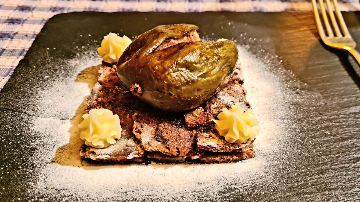 Kletzenbrot-Millefeuille auf einem Schieferbrett angerichet: Schichten von dünnem Kletzenbrot und weißer Pralinenschicht, darauf noch Tupfer dieser Pralinenschokolade und die gebratene Feige
