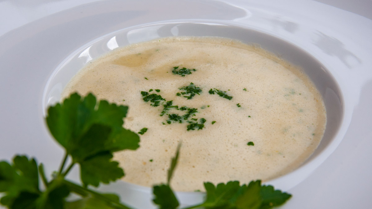 Auf dem Foto: Die Lauchsuppe mit Polenta in einem Suppenteller, darauf gehackte Petersilie, im Vordergrund ein paar Blätter Petersilie