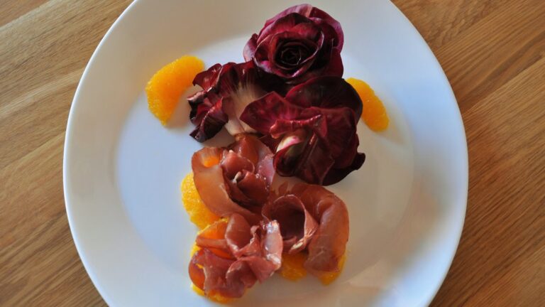 Rosa di Gorizia mit Orangenfilets und Bresaola-Röschen auf einem weißen Teller