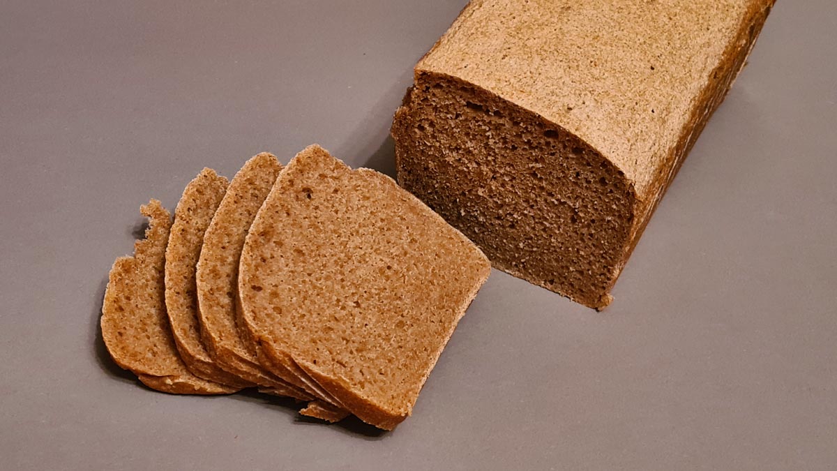 Das Bild zeigt das Vollkornbrot mit Dinkelkeimen, es ist ein Kastenbrot, das angeschnitten wurde. Man sieht die Vollkornkrume und die Kruste des Brotes.