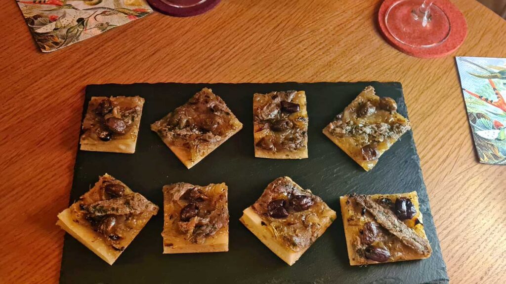 Die Pissaladière aufgeschnitten für den Aperitif - zu sehen sind Teigrechtecke mit der Zwiebelauflage, den Oliven und den Sardellen