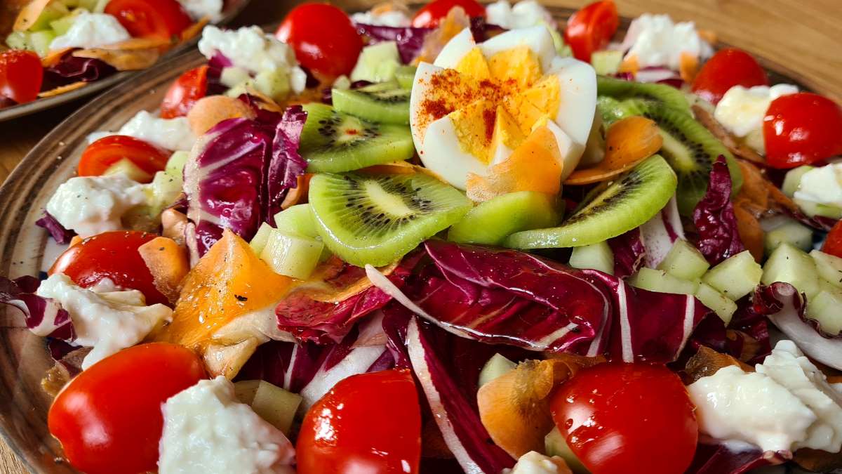 Der Salat in Großaufnahme, man sieht die Stücke vom Radicchio di Verona, auch Kiwis, Tomaten, Karotten, Sfilacci di Mozzarella und ein aufgeschnittenes Ei.