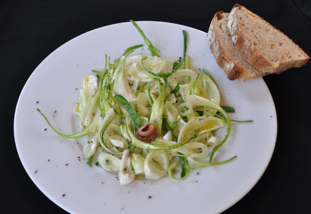 Ein Teller mit der angerichteten "Puntarella alla Romana", zwei Scheiben von italienischem Landbrot am Rand des Tellers