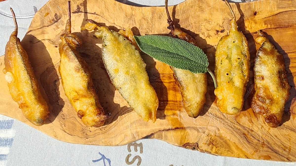 Frittierte Salbeiblätter auf einem Holzbrett aufgereiht, darüber ein frisches Blatt Salbei