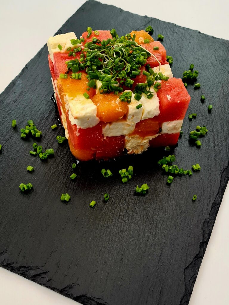 Würfel von Wasser- und Honigmelone und von Feta sind zu einem großen Salatwürfel in den Farben orange, rot und weiß zusammengestellt
