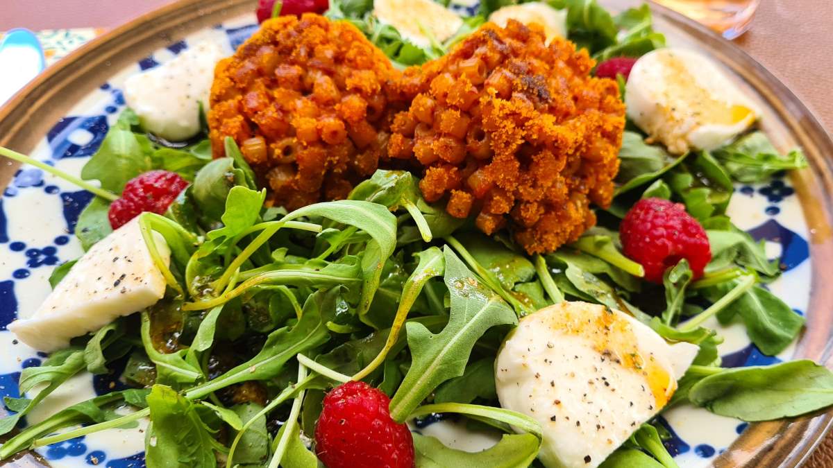 Ein Teller mit Rucolasalat mit Timballini, ein paar Himbeeren und Mozzarella-Scheiben.