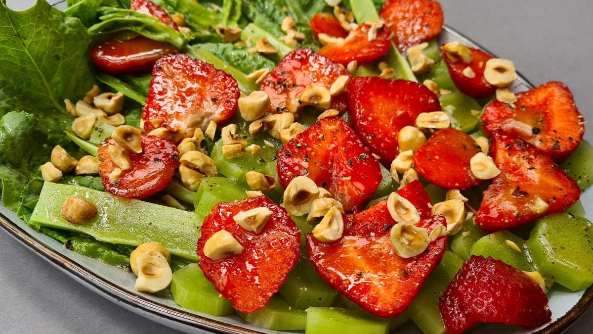 Herrliche Farben: Bunter Keulensalat angerichtet mit halbierten Erdbeeren und gehackten Haselnüssen auf dem grünen Keulenblättern und -stielen
