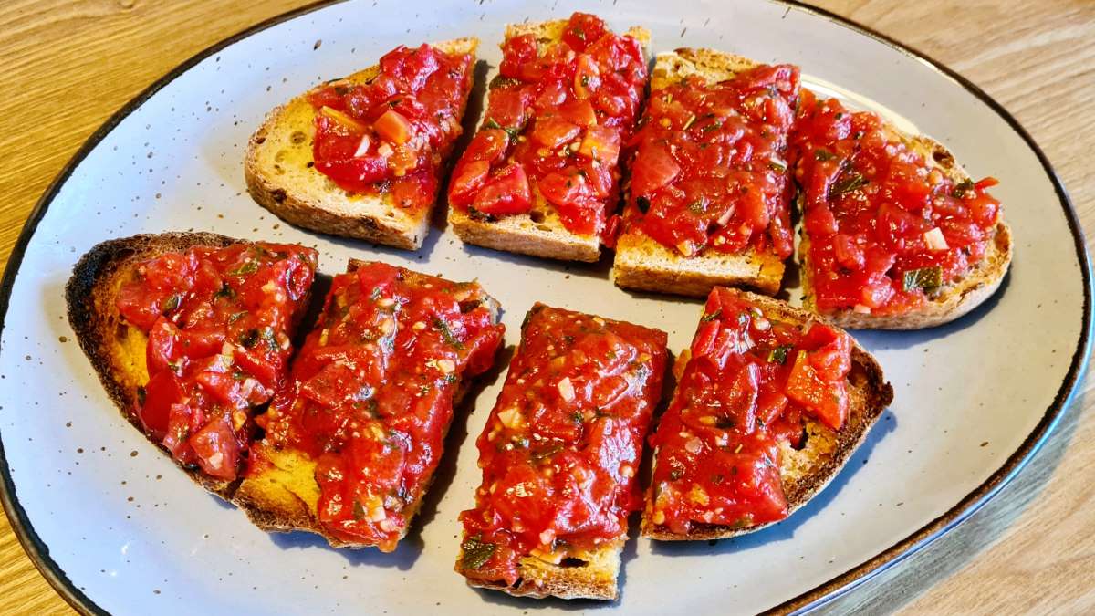 Auf dem Teller sieht man Tomaten Bruschetta, zwei Scheiben getoastetes Brot, in Stücke geschnitten, die gehackten und gewürzten Tomaten darauf. 