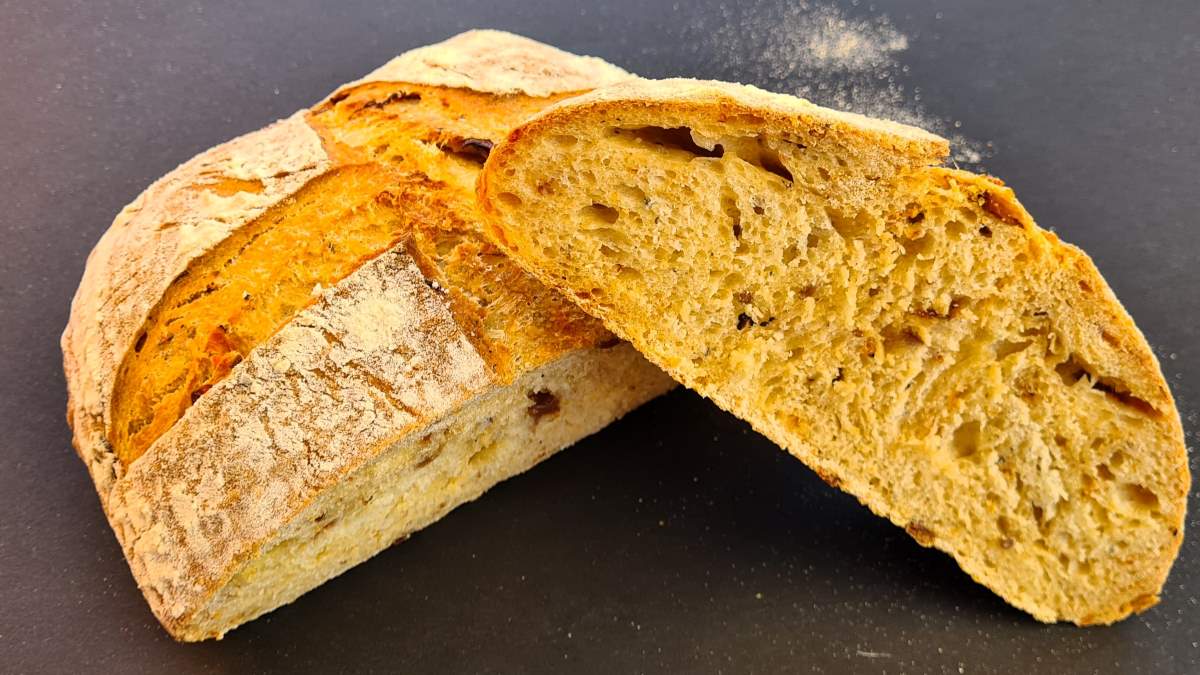 Ein Laib Tomatenbrot, aufgeschnitten: Man sieht die rösche Kruste und die gelbliche Krume mit Tomatenstückchen darin.