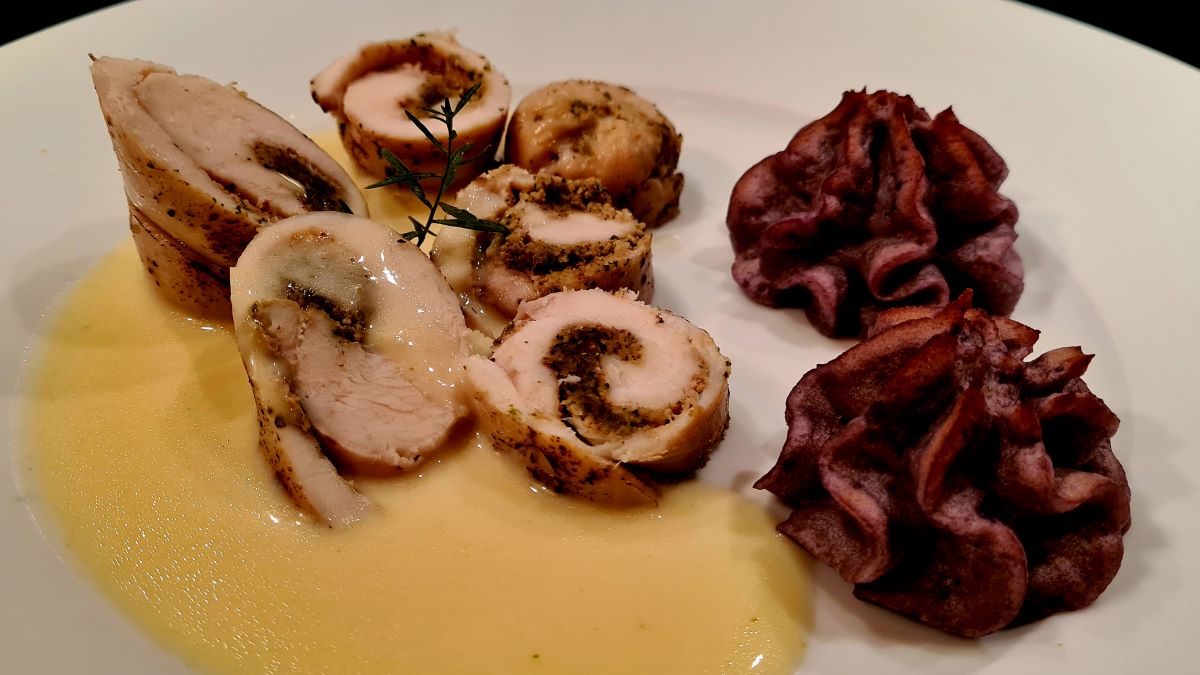 Gefüllte Hühnerrollen mit Walnussorangen-Pesto: Auf dem Teller liegen Scheiben der Hühnerrolle an einer Estragonsauce, daneben Törtchen von Trüffelkartoffeln.