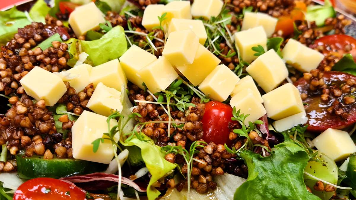 Knuspriger Buchweizen-Salat: Hier sieht man das Gericht angerichtet, die grünen Blätter, die Gurken- und Tomatenstücke sowie den knusprigen Buchweizen. Ergänzt wurde auf diesem Foto der Salat mit Emmentaler Käsewürfel