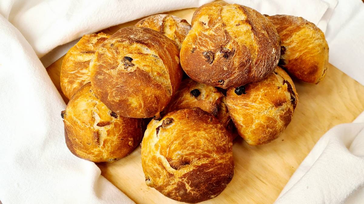 Man sieht die gebackenen Kefir-Rosinen-Brötchen auf einem Holzbrett, eingepackt in Brotleinen.