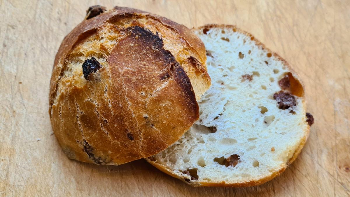 Das Bild zeigt ein Kefir-Rosinen-Brötchen in Großaufnahme, angeschnitten, so dass man nicht nur die knusproge Oberfläche, sondenr auch die weiche Krume mit den Rosinen sehen kann.