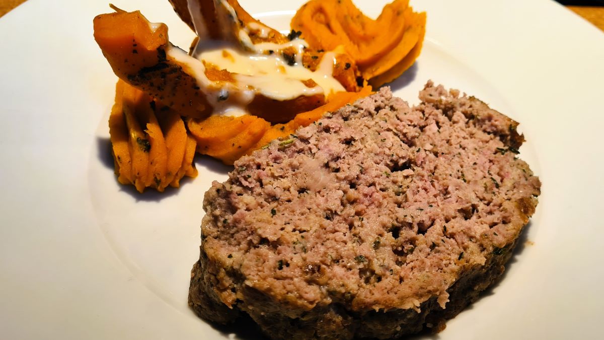 Das Bild zeigt eine Scheibe Polpettone mit gebratenen und pürierten Kürbis auf einem weißen Teller, auf den Kürbisvariationen ist eine Gorgonzola-Sahne-Creme angerichtet.