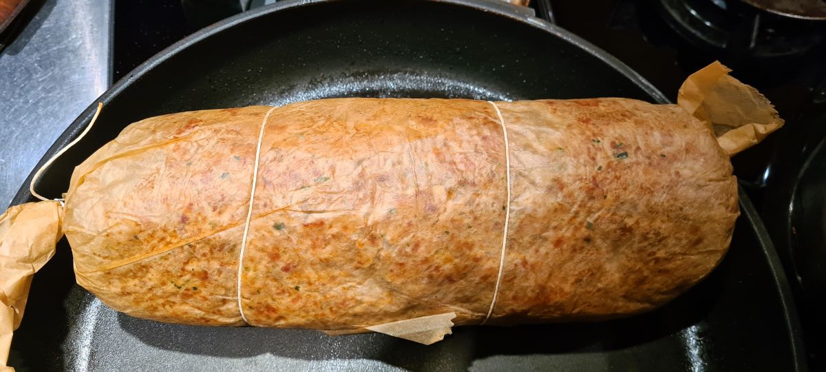 Das Bild zeigt den Polpettone, eingepackt in Backpapier, in der Pfanne, worin er angebraten wird