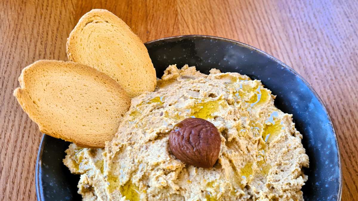 Maroni-Hummus: Das Bild zeigt eine Schüssel mit der Creme, darauf eine gegarte Esskastanie; zwei Crostini sind in das Hummus eingesteckt.