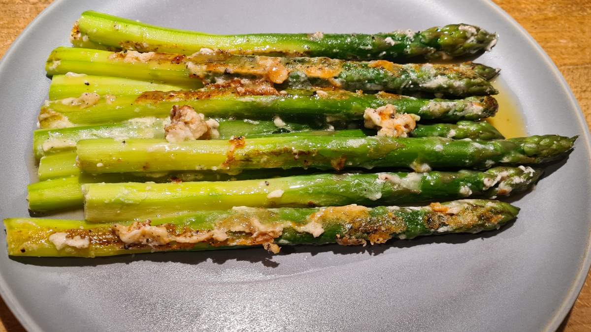 Spargel mit Parmesan: Das Bild zeigt einen grauen Teller, auf dem grüner Spargel mit Butter, Parmesan und geröstetem Eischnee angerichtet ist.