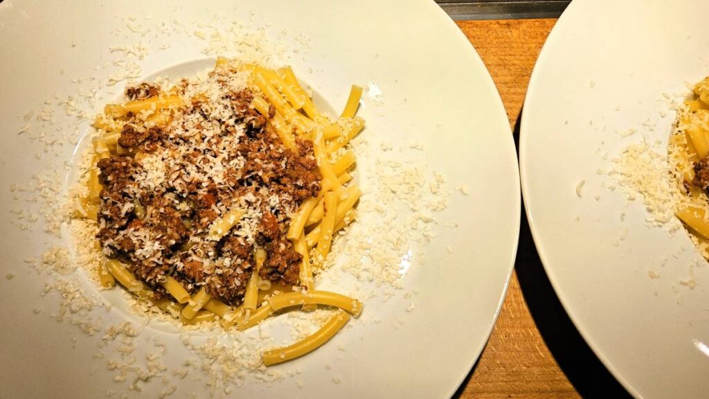 Das Foto zeigt zwei Teller mit Maccaroni und Bolognese, daruf geriebener Parmesan