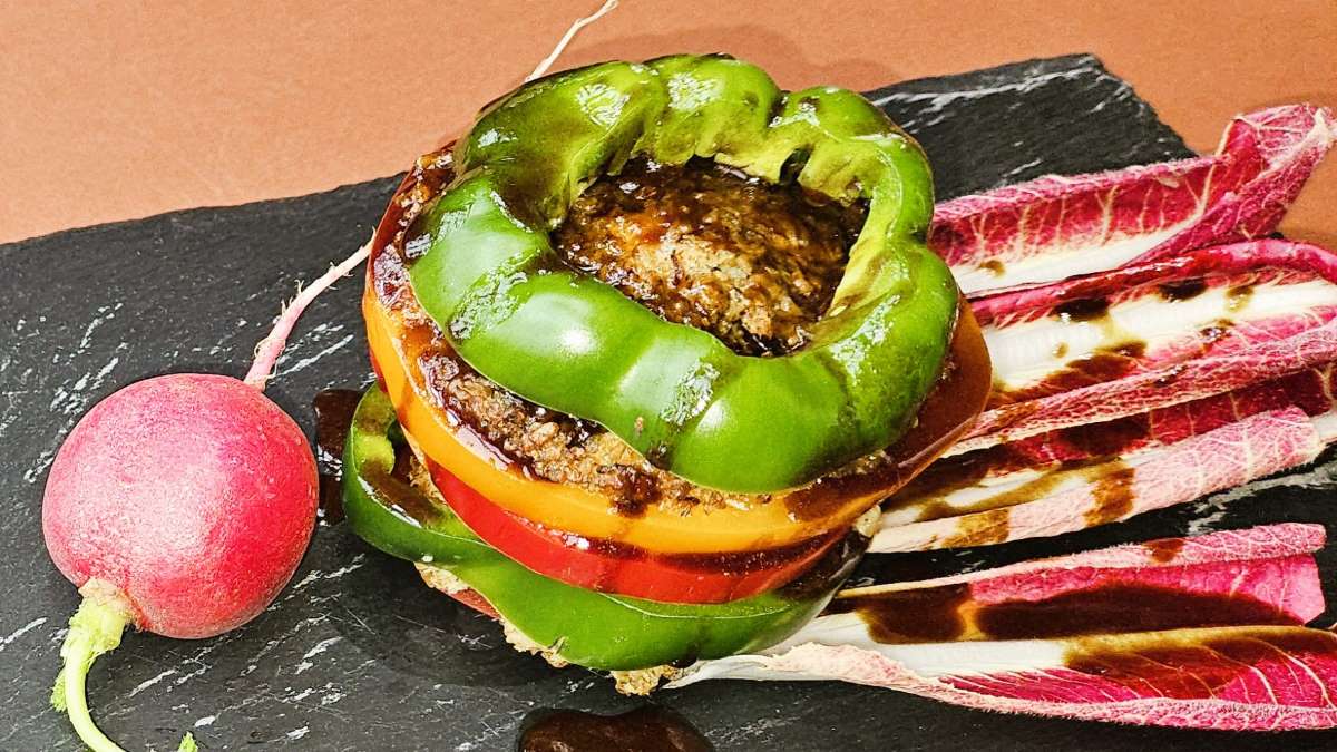 Grünkern-Millefeuille, das Bild zeigt (Perspektive von oben) die Schichten aus grünem, gelbem und rotem Paprika sowie den Scheiben aus dem Grünkern-Laibchen, links liegen rote Chicorée-Blätter, rechts ein Radieschen.