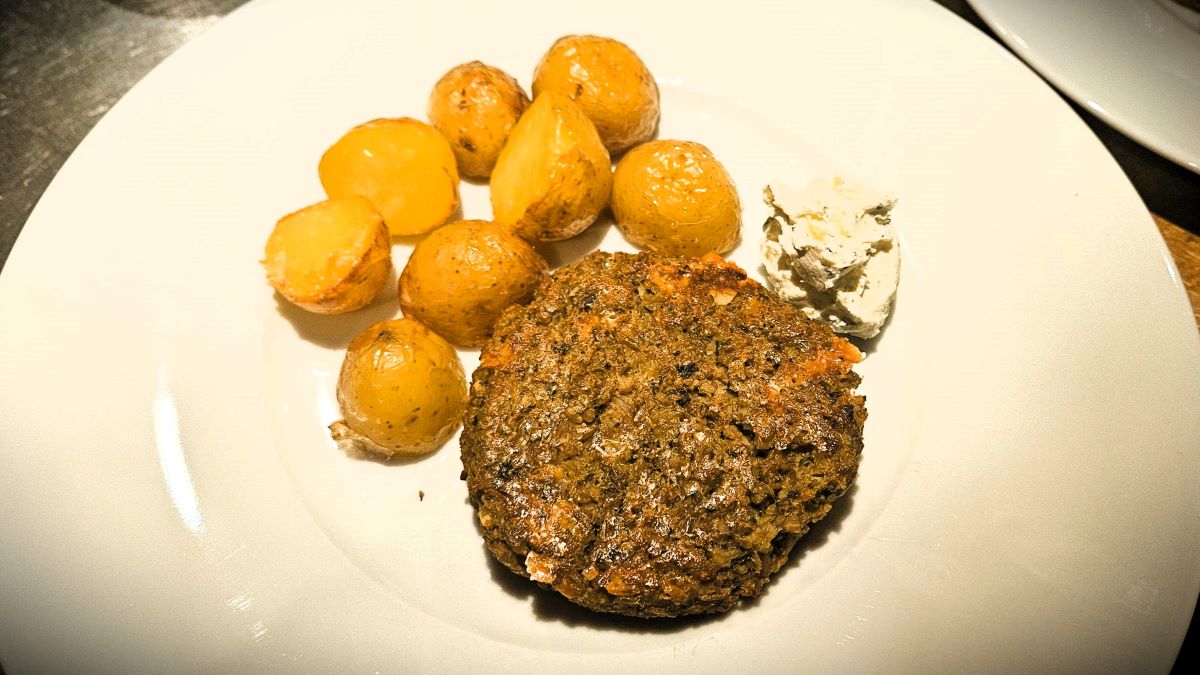 Grünkernlaibchen angerichtet auf einem weißen Teller mit Bratkartoffeln und einem Klacks Kräutercremefraiche.
