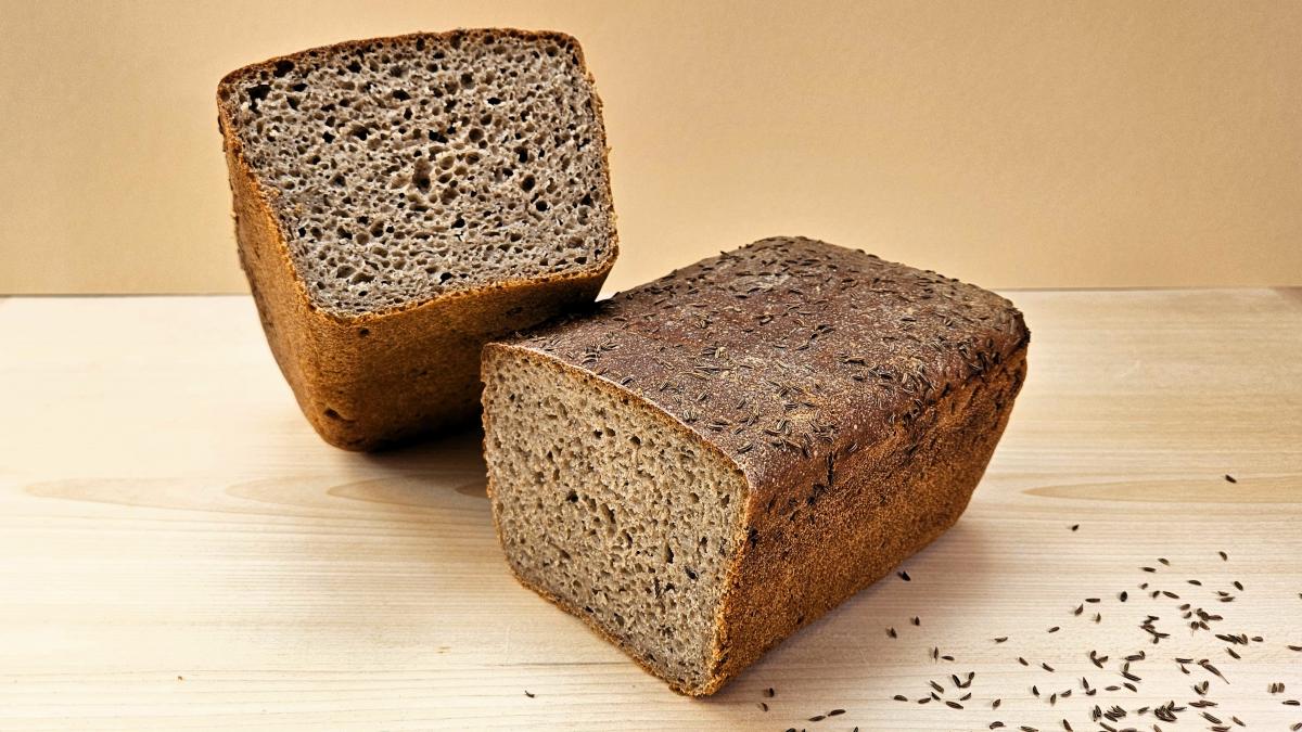 Kümmelkastenbrot: Das Kastenbrot liegt angeschnitten auf einem Holzbrett, man sieht die Kruste mit dem Kümmeltopping und die typische Sauerteigkrume.
