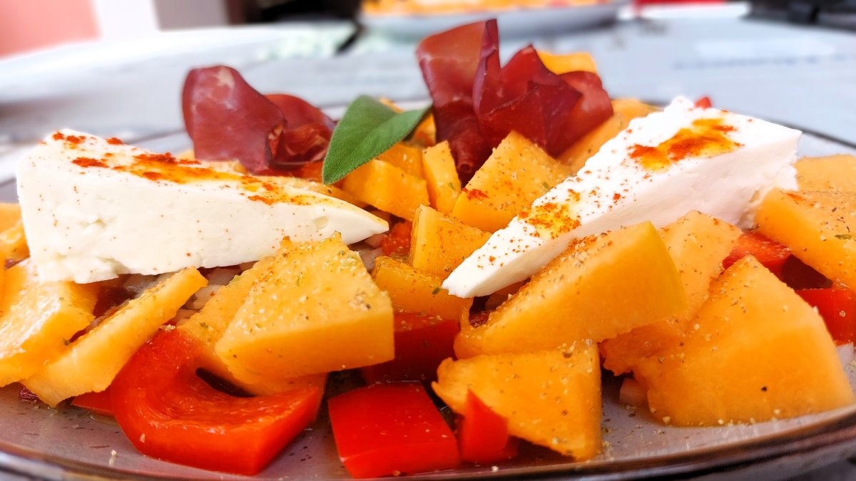 Italienischer Salat in Großaufnahme: Rote Paprika und gelbe Melonenstückchen, weißer Panarello-Käse , dunkelrote Bresaola und Kräuterblätter verbinden sich zu einem sommerlichen Genuss