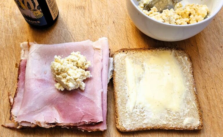 Croque Monsieur - die Vorbereitung: Das Bild zeigt zwei Toastscheiben, links belegt mit Schinken und Käsecreme, rechts mit Butter bestrichen
