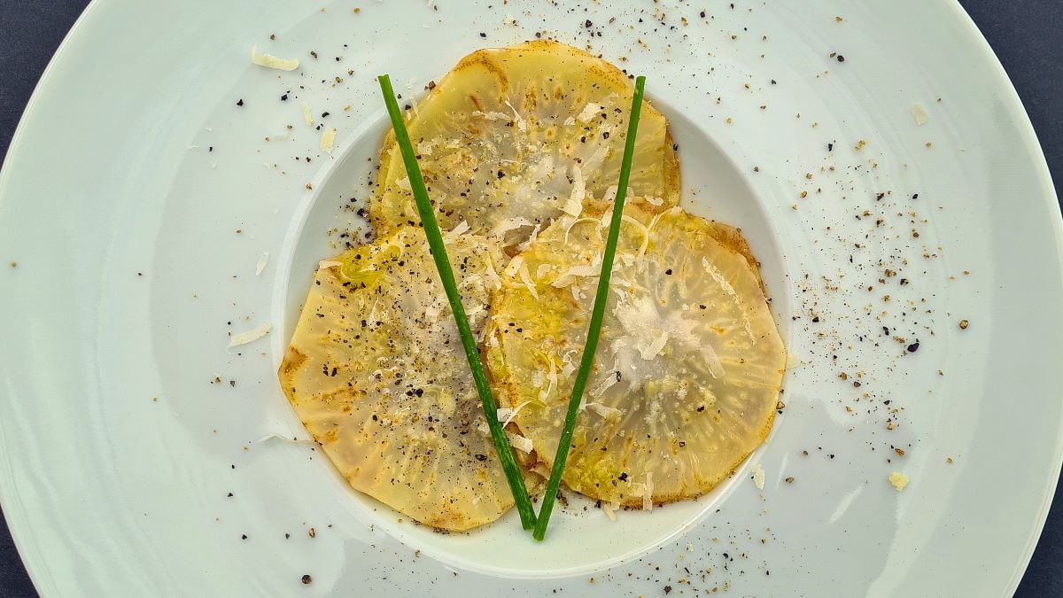 Auf dem Bild sind drei Zeller-Ravioloni von oben zu sehen, darüber geriebener Parmesan und gekreuzte Schnittlauchhalme