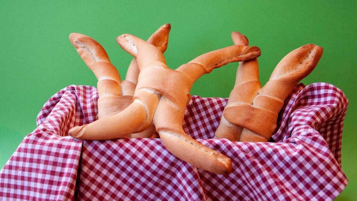In einem Körbchen, ausgelegt mit rot-weiß-kariertem Tuch liegen drei Pane Ferrarese, eines ist komplett sichtbar mit seinen vier Zipfeln, Locken oder Hörnern. Der Hintergrund ist grün.