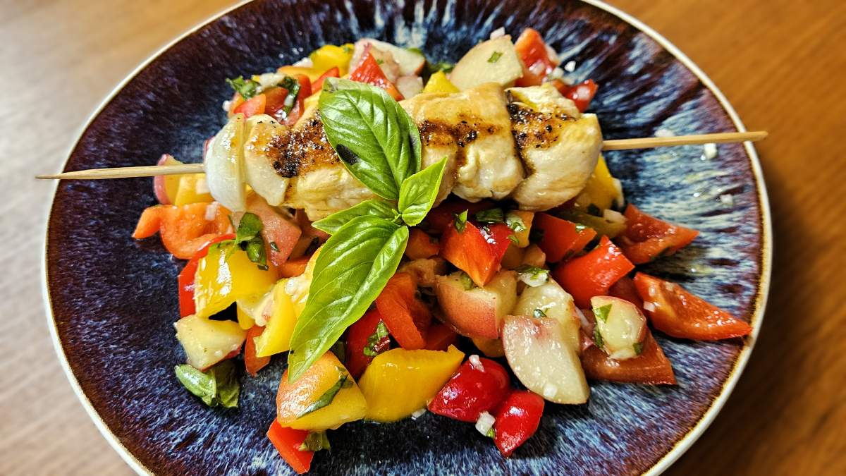 Paprika-Pfirsich-Salat auf einem blauen Teller: Zu sehen sind die Zutaten - Paprika, Pfirsiche, Zwiebel, Basilikum - und der Hühnerspieß mit der Marinade.
