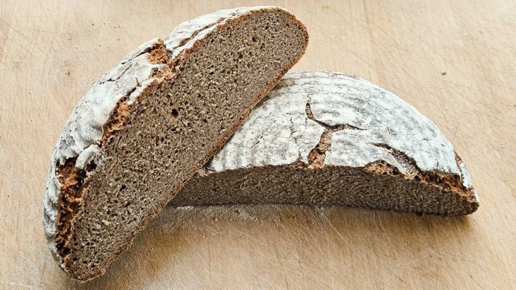 Der Anschnitt vom Vollkornbrot aus Champagnerroggen. Der Brotlaib ist halbiert, die dunkle Krume ist dicht und saftig.